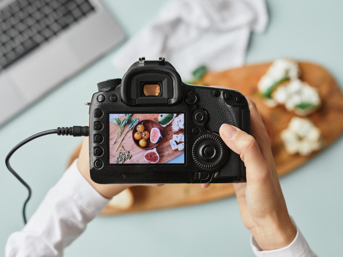 top-view-close-up-food-photographer-holding-digital-camera-with-image-screen-while-working-home-studio-copy-space (1)